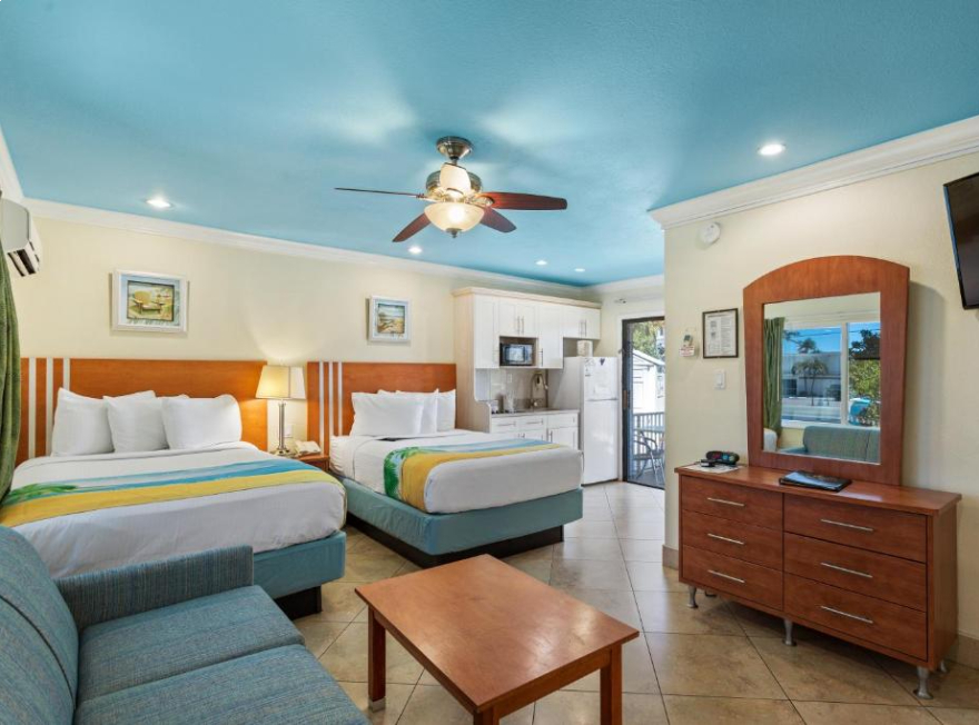 A wide view of a hotel suite with two double beds, a kitchenette, a sofa, and a coffee table.