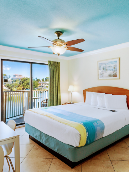 A well-furnished bedroom with a bed, desk, chair, table, and a balcony, located in a bay palms waterfront resort.